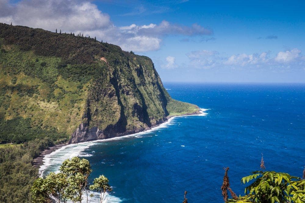 Lush green cliffside overlooking a blue ocean under a partly cloudy sky.