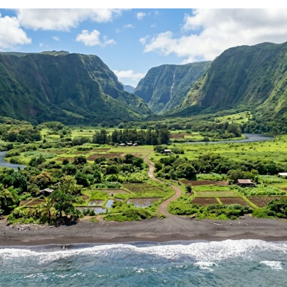 Lush valley with mountains, river, fields, and a sandy beach under a cloudy blue sky.
